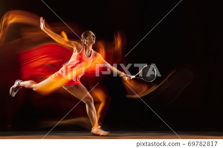 Professional female tennis player isolated on black studio background in mixed light Professional female tennis player isolated on black studio background in mixed light 69782817