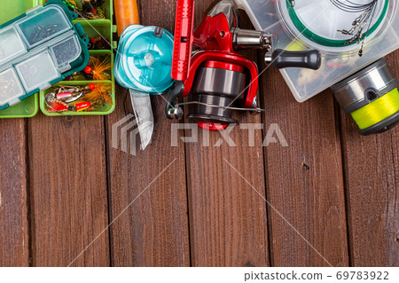Different fishing tacles with lures and reels on wooden brown background with place for text. Different fishing tacles with lures and reels on wooden brown background with place for text. 69783922