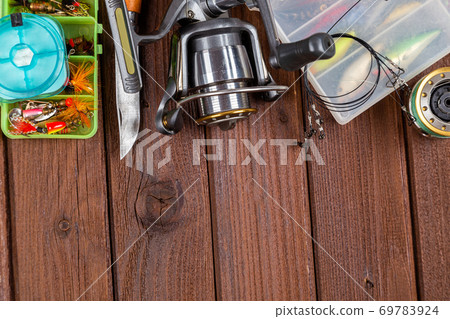 Different fishing tacles with lures and reels on wooden brown background with place for text. Different fishing tacles with lures and reels on wooden brown background with place for text. 69783924