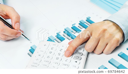 Finance. Female Hands with calculator on financial graphs on desk Finance. Female Hands with calculator on financial graphs on desk 69784642