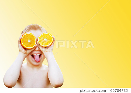 child with halves of oranges on eyes. happy child having fun and showing tongue. the boy is holding fruit on a light blue background child with halves of oranges on eyes. happy child having fun and showing tongue. the boy is holding fruit on a light blue background 69784783
