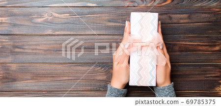 Girl Hands holding craft paper gift box with as a present for Christmas or other holiday on dark wooden background, top view with copy sppace Girl Hands holding craft paper gift box with as a present for Christmas or other holiday on dark wooden background, top view with copy sppace 69785375