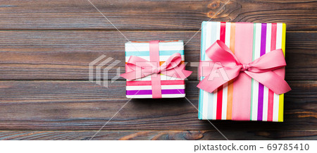 Beautiful gift box with a colored bow on the dark wooden table. Top view banner with copy space for you design Beautiful gift box with a colored bow on the dark wooden table. Top view banner with copy space for you design 69785410