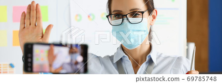 Business woman in protective mask say hallo on smartphone camera portrait Business woman in protective mask say hallo on smartphone camera portrait 69785748