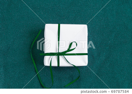 Gift in a white package on a green background. Gift in a white package on a green background. 69787584