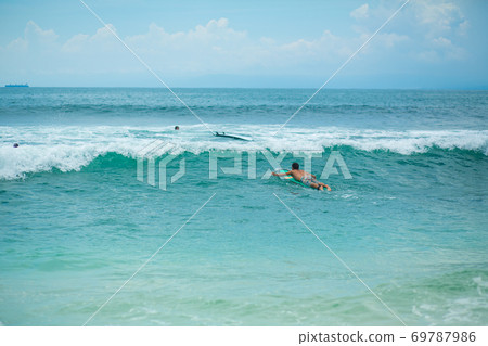 The guy is swimming on the surf board on the ocean. Healthy active lifestyle in summer vocation. The guy is swimming on the surf board on the ocean. Healthy active lifestyle in summer vocation. 69787986