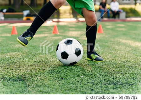 Persistent teen soccer player kicking ball on field. Close up feet of footballer kicking ball on green grass. 69789782