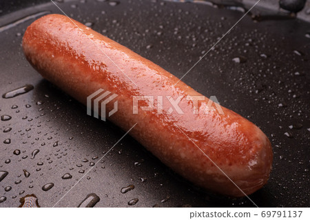 one sausage fried in a pan with drops of oil.  69791137
