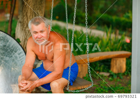 tanned elderly man sitting on swings in his garden tanned elderly man sitting on swings in his garden 69793321