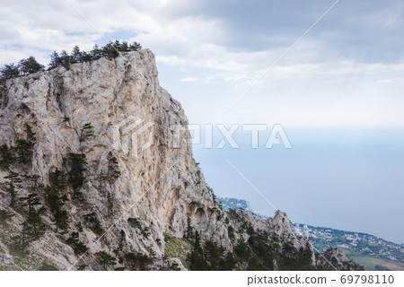 A picturesque mountain covered with trees on the background of a misty valley with the sea far below A picturesque mountain covered with trees on the background of a misty valley with the sea far below 69798110