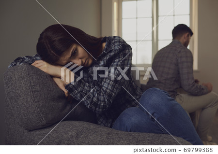 A young couple quarreling while sitting on a sofa in a room. A young couple quarreling while sitting on a sofa in a room. 69799388
