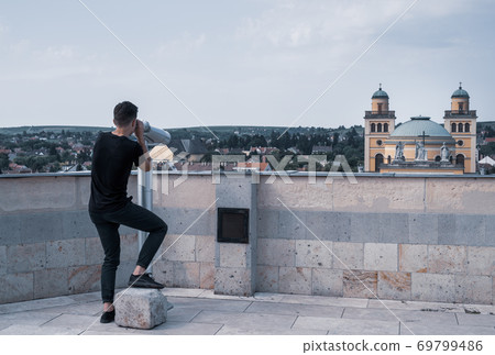Young man on observation deck looking through telescope on old hungerian town Eger 69799486