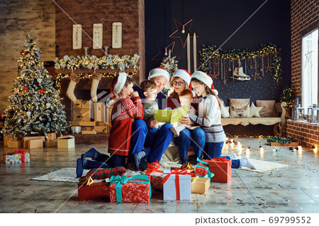 Grandparents reading a book with a child in the room with tree on Christmas Day. 69799552