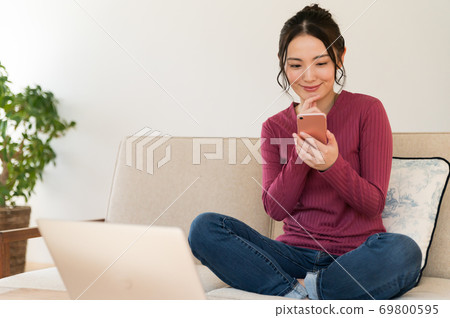 A woman operating a smartphone on the sofa during telework A woman operating a smartphone on the sofa during telework 69800595
