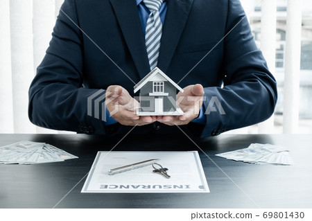 The hand of the real estate agent has a sample house with home insurance documents and keys to present to his clients who have made a purchase. Home insurance sales concept 69801430
