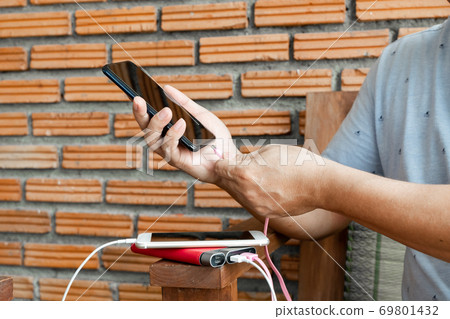 The hand of a man holding a smart phone and a modern Power Bank charger. Put it at the desk, charging the smartphone with a spare battery charger, In a size that sits play chair The hand of a man holding a smart phone and a modern Power Bank charger. Put it at the desk, charging the smartphone with a spare battery charger, In a size that sits play chair 69801432