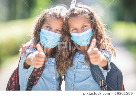 Twin sisters with face masks go back to school during the Covid-19 quarantine and showing thumbs up Twin sisters with face masks go back to school during the Covid-19 quarantine and showing thumbs up 69801599