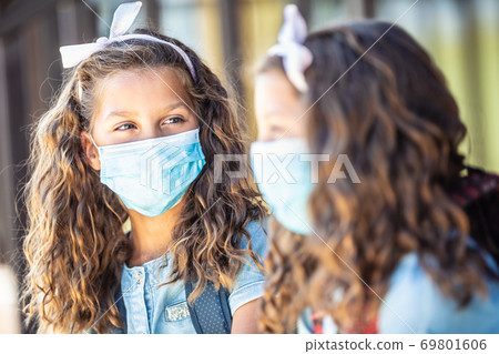 Two young twin sisters classmates with face masks talk on their way to school during the Covid-19 quarantine 69801606