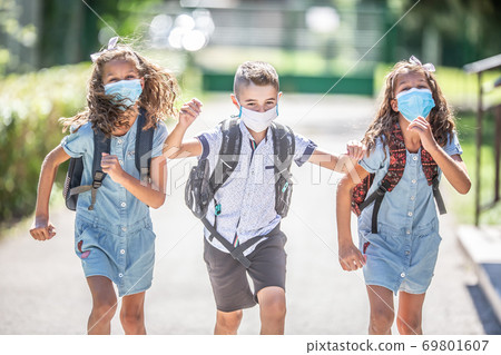 Happy schoolchildren with face masks run from the joy of returning to school during the Covid-19 quarantine 69801607