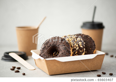 chocolate donuts with glaze in a craft box and black coffee in cups chocolate donuts with glaze in a craft box and black coffee in cups 69803407