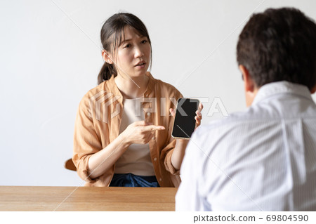 Wife showing her husband a cell phone Wife showing her husband a cell phone 69804590