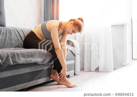 Woman sitting on sofa holds her foot injury, feeling pain. Health care concept Woman sitting on sofa holds her foot injury, feeling pain. Health care concept 69804831