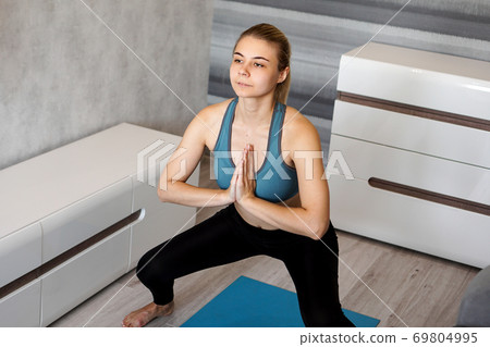 Young woman exercising and doing squats at home Young woman exercising and doing squats at home 69804995