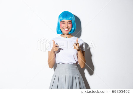 Cheeky japanese girl in blue party wig pointing fingers at camera and smiling, celebrating halloween, standing over white background Cheeky japanese girl in blue party wig pointing fingers at camera and smiling, celebrating halloween, standing over white background 69805402