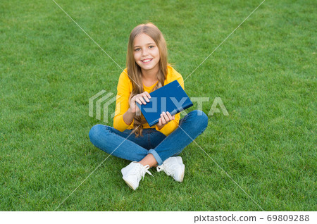 Girl reading book outdoors green lawn background, kid 69809288