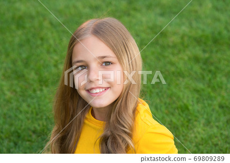 carefree child on green grass. little girl with pleasant smile. kid with cute curly hair 69809289