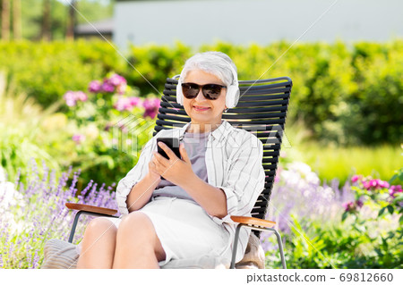 old woman with headphones and smartphone at garden 69812660