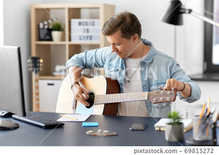 young man playing guitar sitting at table at home young man playing guitar sitting at table at home 69813272