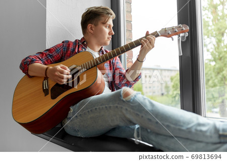 young man playing guitar sitting on windowsill young man playing guitar sitting on windowsill 69813694