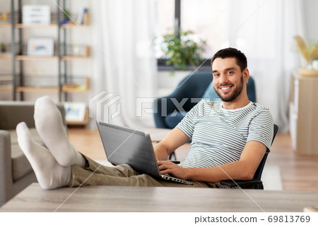 man with laptop resting feet on table at home 69813769