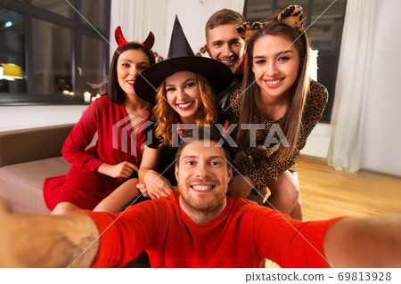 happy friends in halloween costumes taking selfie 69813928