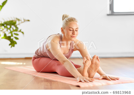 woman doing yoga and seated forward bend at home 69813968