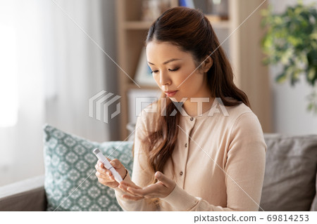 asian woman with glucometer makes blood sugar test 69814253