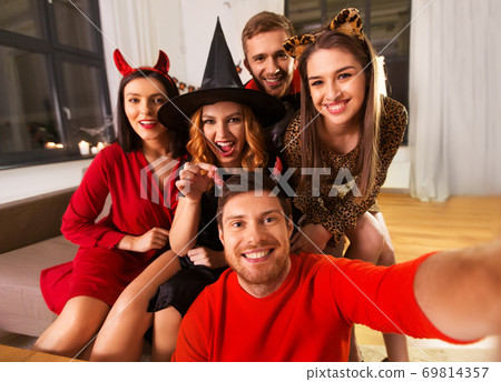 happy friends in halloween costumes taking selfie 69814357