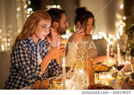 woman with smartphone at dinner party with friends woman with smartphone at dinner party with friends 69814635