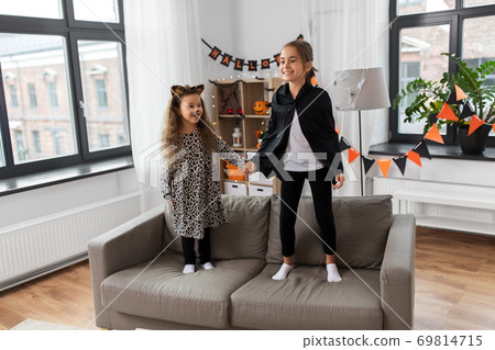 girls in halloween costumes jumping on sofa 69814715