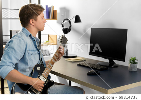 young man with computer playing guitar at home young man with computer playing guitar at home 69814735