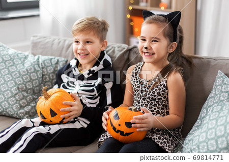 kids in halloween costumes with pumpkins at home 69814771