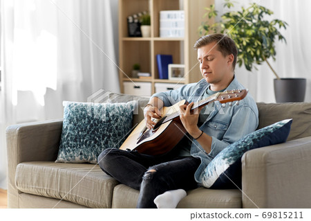 young man playing guitar sitting on sofa at home 69815211