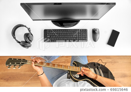 young man with computer playing guitar at table young man with computer playing guitar at table 69815646