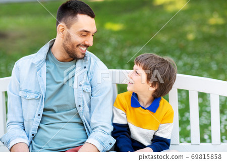 father with son sitting on park bench and talking father with son sitting on park bench and talking 69815858