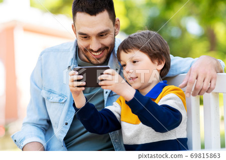 father and son with smartphone at park father and son with smartphone at park 69815863