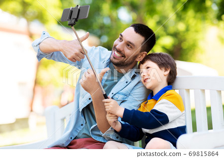 father and son taking selfie with phone at park father and son taking selfie with phone at park 69815864