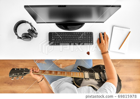 young man with computer and guitar at table young man with computer and guitar at table 69815978