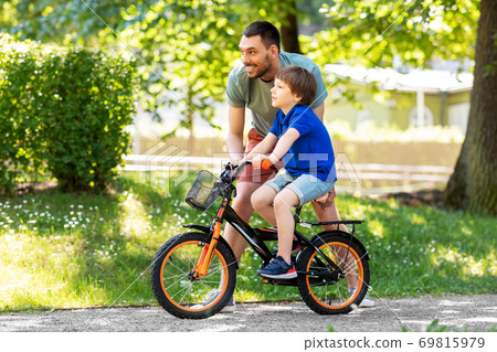 father teaching little son to ride bicycle at park father teaching little son to ride bicycle at park 69815979
