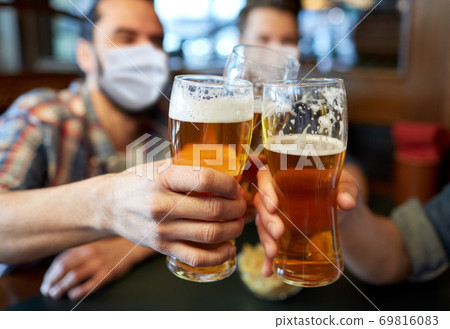 male friends in masks drinking beer at bar or pub 69816083